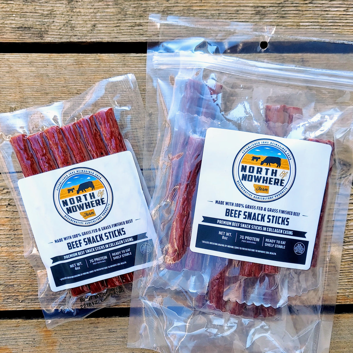North of Nowhere Farms offers two different package types for their grassfed, grass-finished beef sticks: a 4-ounce vacuum-sealed 6-pack and an 8-ounce resealale pouch of 8 individually vacuum-sealed beef sticks. Packages shown on barnwood background.